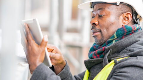 Man wearing a hard hat working on a tablet at an indoor construction site